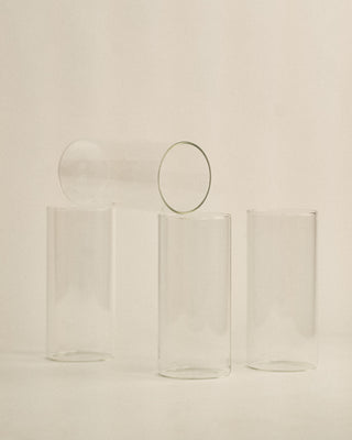 Four clear glass tumblers with circular handles on a beige background
